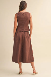 A woman wears a sleeveless brown satin midi dress with pleated waist flare and back seam detail