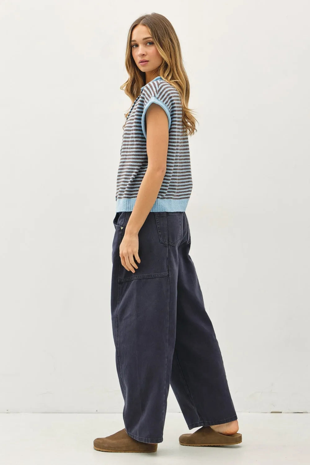 A woman wears a mini striped piper button sleeveless knit top with navy and light blue stripes paired with dark denim pants