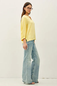 A woman wears a soft yellow notched y-neck volume sleeve blouse with three-quarter loose-fitting sleeves and v-neckline