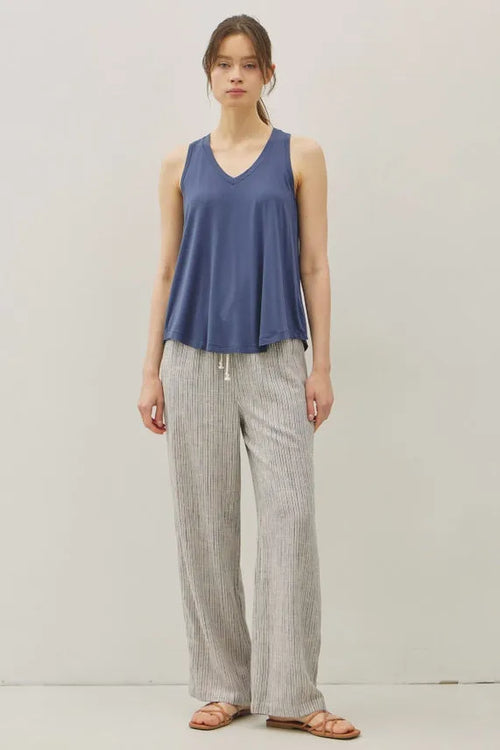A woman wears a soft navy blue sleeveless top paired with stripy linen wide leg pants in a relaxed fit style