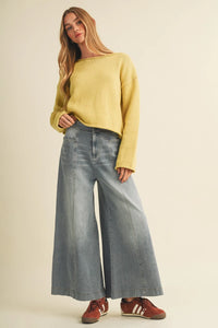 A woman wears yellow ribbed knit sweater with vertical seam wide light-wash wide leg denim trousers and red sneakers