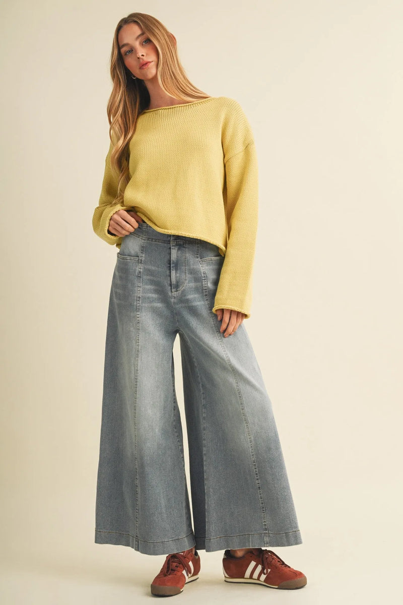 A woman wears yellow ribbed knit sweater with vertical seam wide light-wash wide leg denim trousers and red sneakers