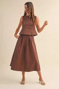 A woman wears a brown linen pleated waist flare midi skirt paired with a sleeveless peplum top