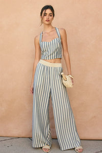 A woman wearing light blue and white stripe print waist wide leg pants with a matching crop top and woven clutch