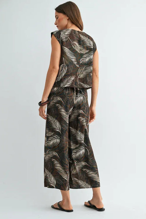 A woman wears leaf print elastic wide-leg pants and sleeveless top in dark brown fabric with white feather print