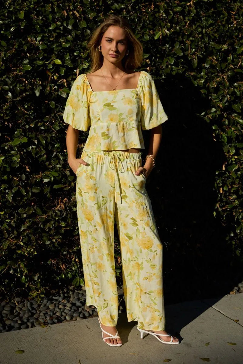 A woman wearing midi rise elastic wide pants with an elastic waist band in soft yellow and green floral tones