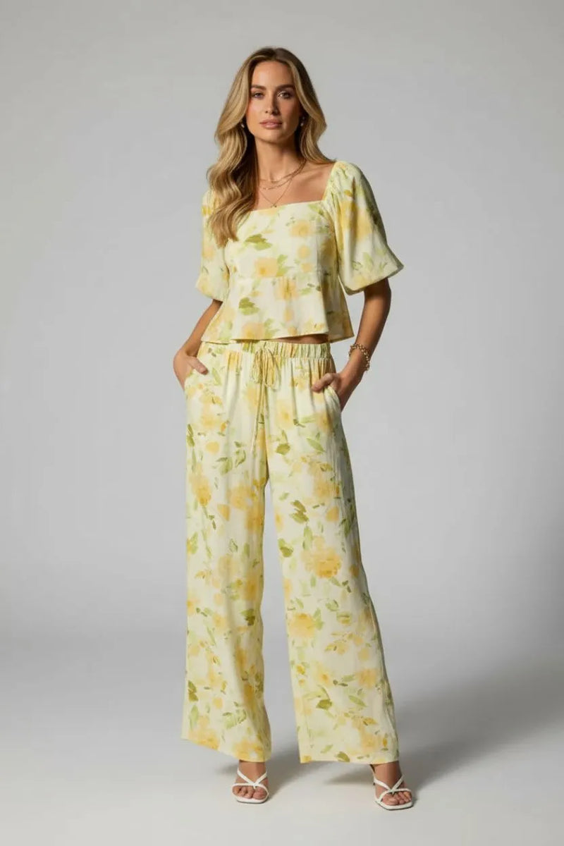 A woman wears light yellow midi rise elastic waist band wide pants with matching floral top featuring flutter sleeves