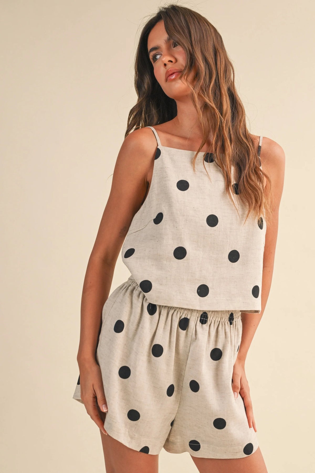 A woman wearing a light beige polka dot linen sleeveless top with matching two-piece set in black dots