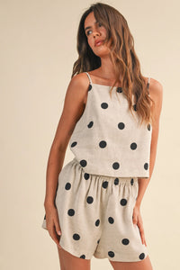 A woman wearing a light beige polka dot linen sleeveless top with matching two-piece set in black dots