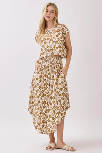 A woman wearing a cream smocked waistband midi skirt with gold floral print paired with a matching short-sleeved top