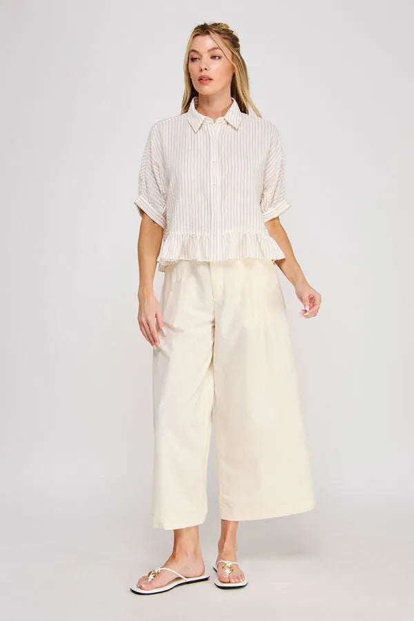 A woman wears a white and light gray button down striped ruffle detail top from shop daisy women’s boho chic clothing