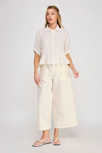 A woman wears a white and light gray button down striped ruffle detail top from shop daisy women’s boho chic clothing