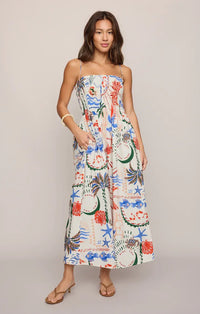 A woman wearing a white sleeveless cornelia getaway maxi dress with colorful seashell and ocean print on thin straps