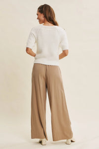 A woman wears beige step washed wide leg pants paired with a white short-sleeved knit sweater with shoulder detailing
