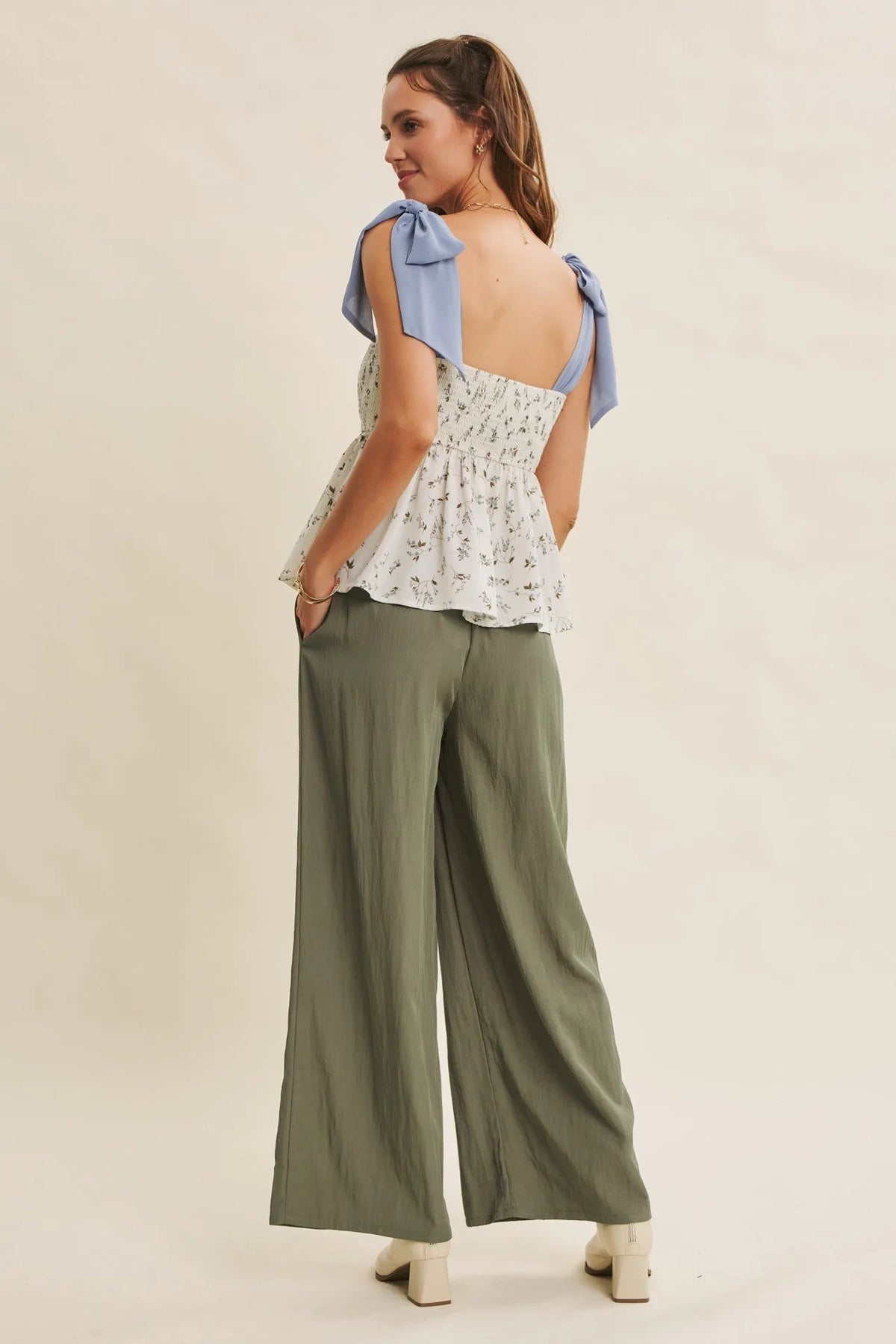 A woman wears olive green step washed wide leg pants paired with a white floral top with light blue bow straps