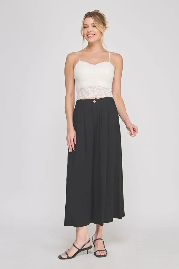 A woman wearing a white floral lace scallop edge sweetheart bralette paired with high-waisted black wide-leg trousers