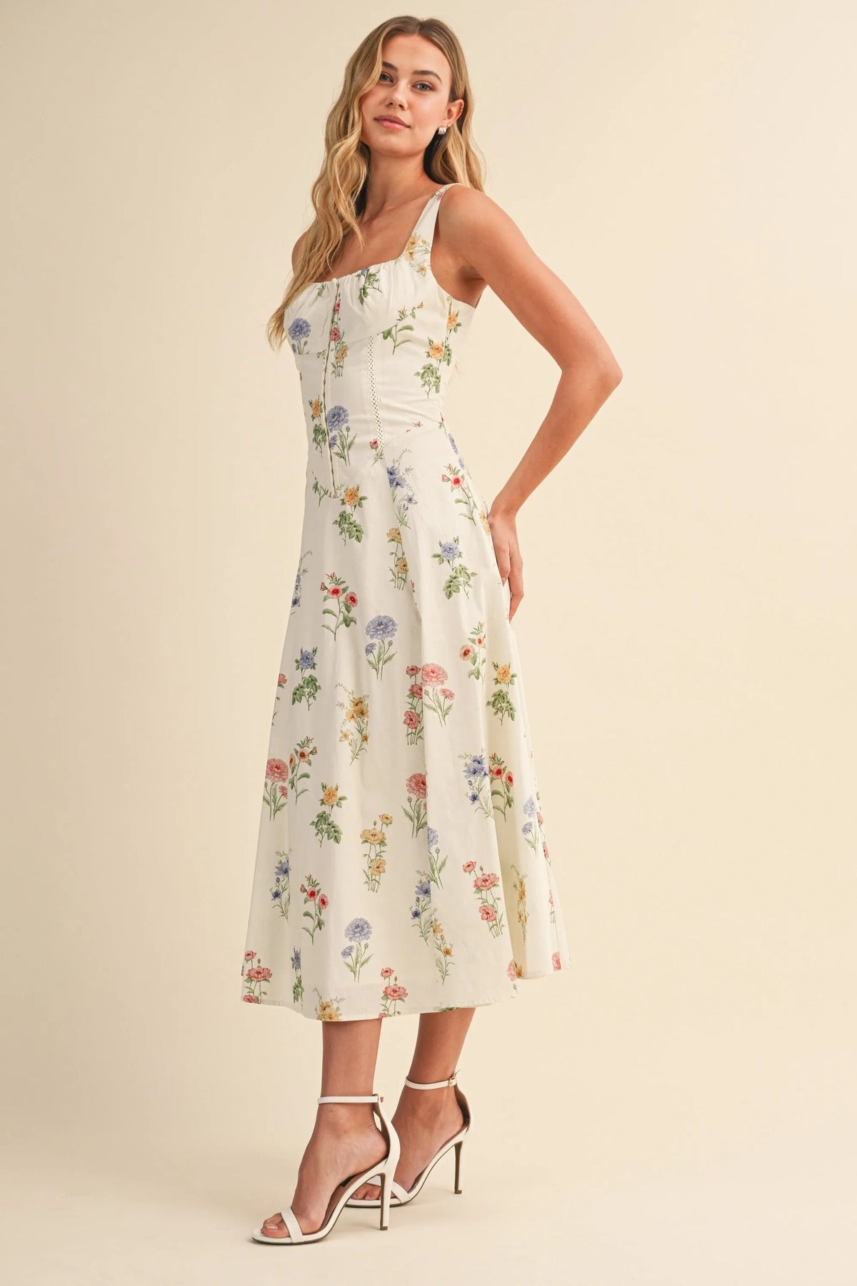 A woman wears a white floral tie back lace up midi dress with colorful blossoms in women’s boho chic clothing