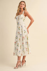 A woman wears a white floral tie back lace up midi dress with colorful blossoms in women’s boho chic clothing