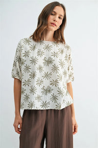 A woman wearing a white flower print dolman blouse with olive green starburst print dolman sleeve details