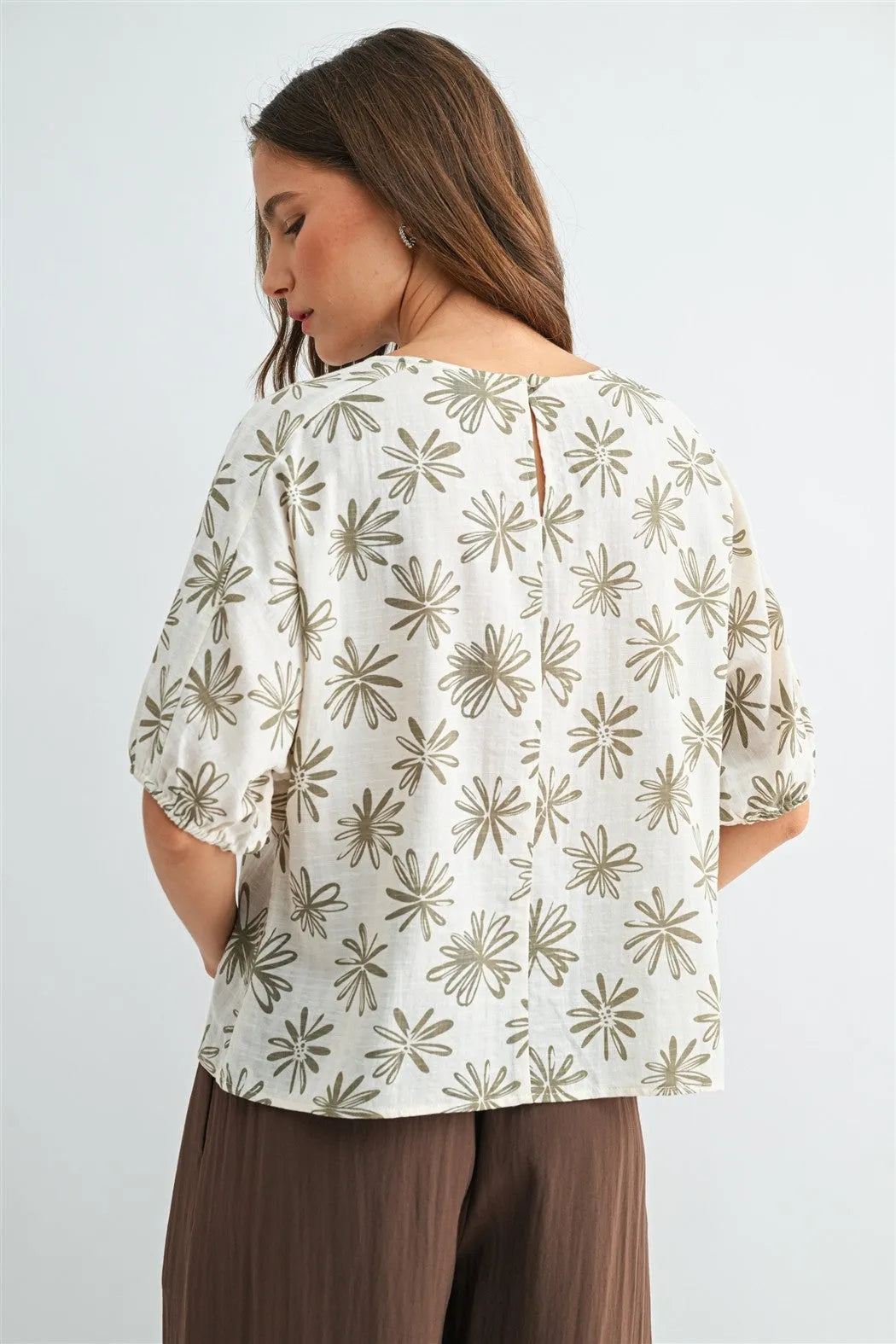 A woman wears a white flower print dolman blouse with olive green starburst patterns and puffed sleeves