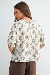 A woman wears a white flower print dolman blouse with olive green starburst patterns and puffed sleeves