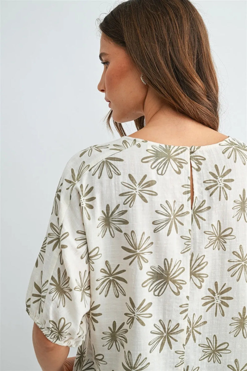 A woman wears a white flower print dolman blouse with olive green floral patterns and puffed sleeves