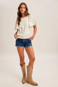 A woman wears a white wing sleeve blouse with puffed sleeves and subtle stitching details in a loose fit