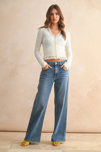 A woman wears a white lace contrasted knitted cropped cardigan with long sleeves and button closures paired with jeans