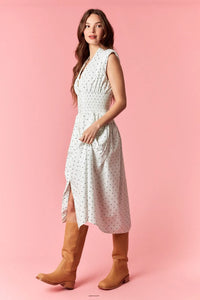 A woman wears a white pin polka dot flare midi dress with v-neck zip-up and fitted waist paired with tan boots