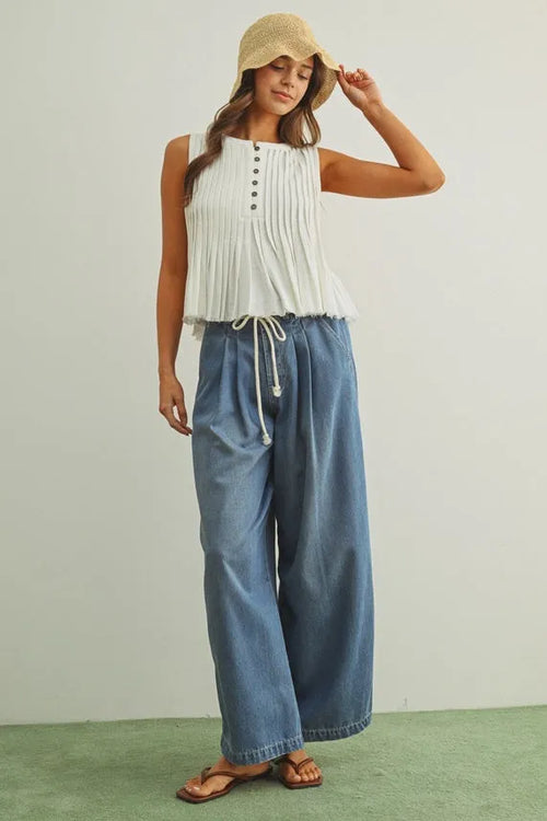 A woman wears wide-leg blue tencel denim pants with a pleated cotton belt and a white sleeveless top