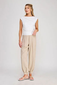 A woman wearing a white sleeveless boat neck scrunch tank top paired with beige loose-fitting tapered pants