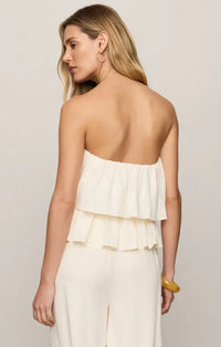 A woman wears a white strapless linen mabel top with layered ruffles and matching wide-leg pants