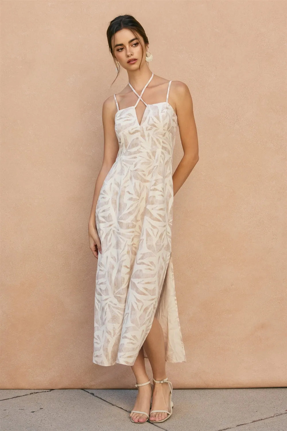 A woman wearing a white tropical leaf v cut maxi dress with thin straps and a side slit