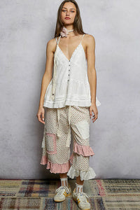 A woman wears a white sleeveless relaxed fit v-neck top with button front ruffles and delicate lace trim
