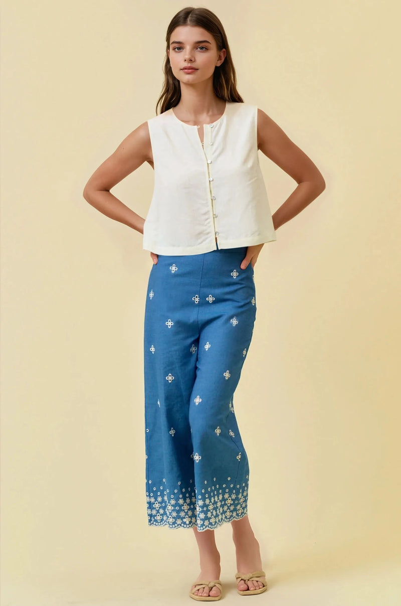 A woman wearing a white viscose blend button front top paired with blue wide-leg pants with white embroidery