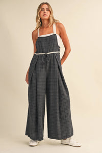 A woman wearing a wide-leg drawcord waistline plaid jumpsuit with white straps and adjustable ankle drawstrings