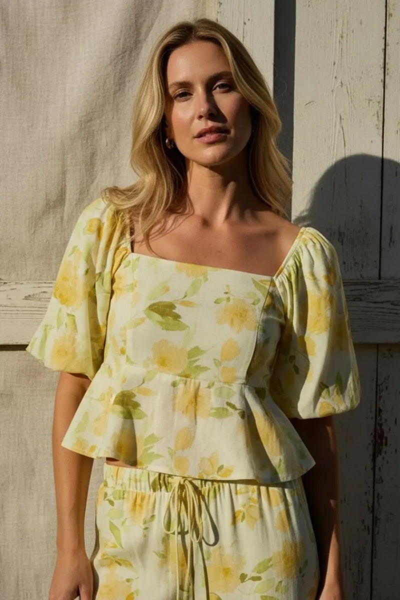 A woman wearing a yellow floral square neck bubble hem peplum blouse with puffed sleeves and matching high-waisted pants