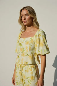 A woman wears a yellow and green floral print square neck bubble hem peplum blouse with puff sleeves