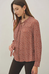 A rust-colored ditsy printed tie front collar blouse with long sleeves and matching tied cuffs in lightweight fabric