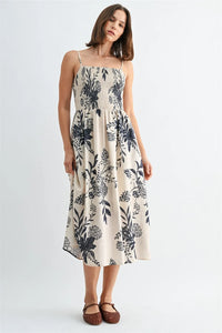 A women’s off-white midi dress with black floral pattern featuring thin spaghetti straps and smock detailing