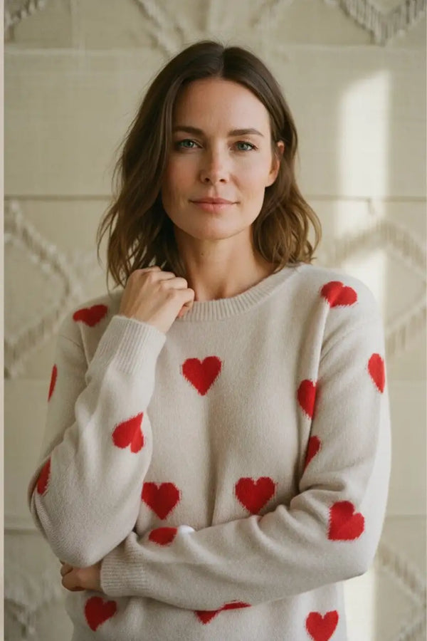 A cozy off-white knit sweater adorned with vibrant red heart patterns.