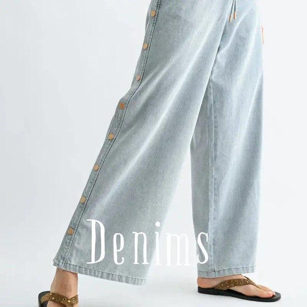 Light-wash denim wide-leg pants featuring a row of tan buttons down the side seam.
