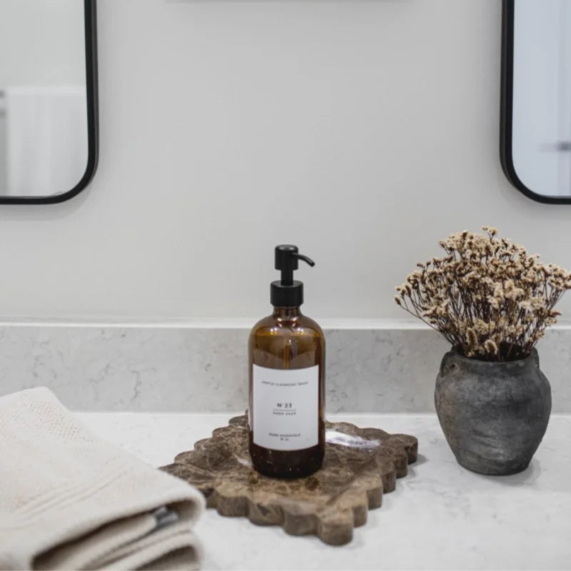 Amber glass hand soap bottle with black cap on rustic wooden tray