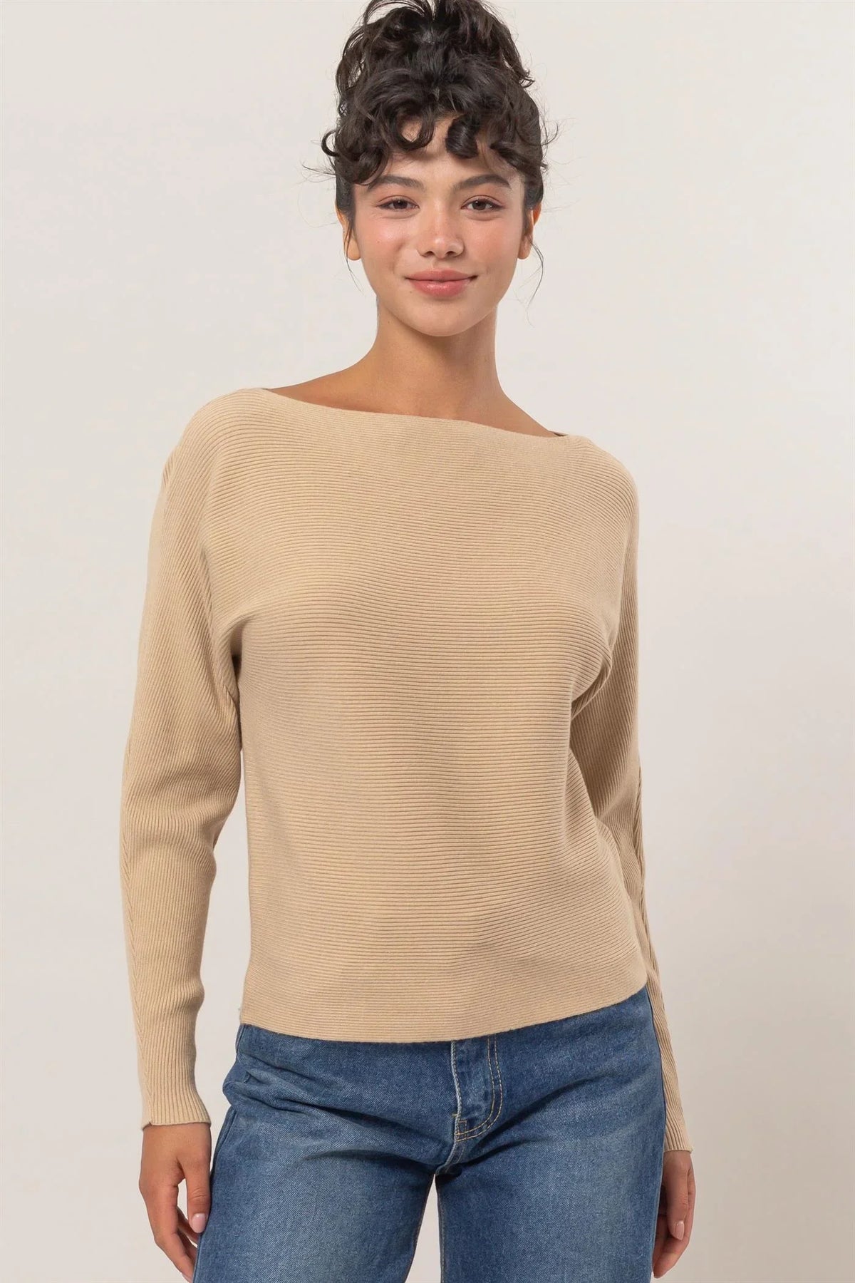 Beige boat-neck long sleeve sweater styled with blue jeans showcasing ribbed texture