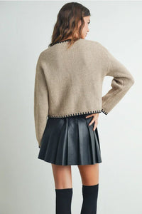 Beige cable knit crewneck cardigan sweater with black trim and ribbed cuffs