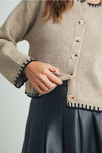 Beige crewneck cardigan sweater with black and white trim, ribbed texture, button closure