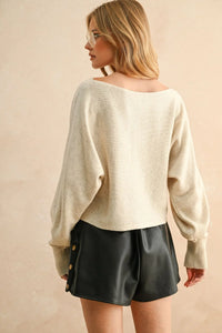 Beige boat neck sweater with long sleeves paired with black faux leather shorts