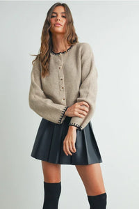 Beige ribbed crewneck cardigan sweater with black trim, navy faux leather skirt