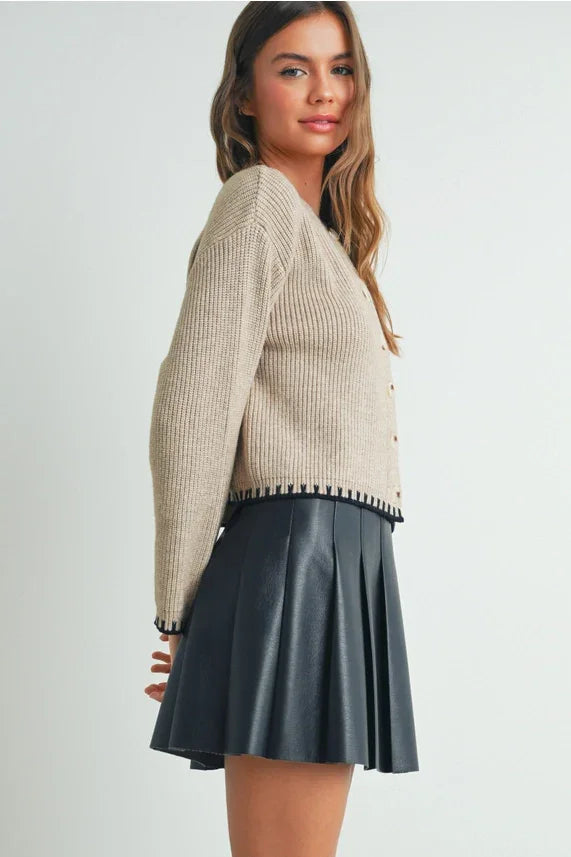 Beige ribbed crewneck cardigan sweater with striped trim and gray faux leather skirt