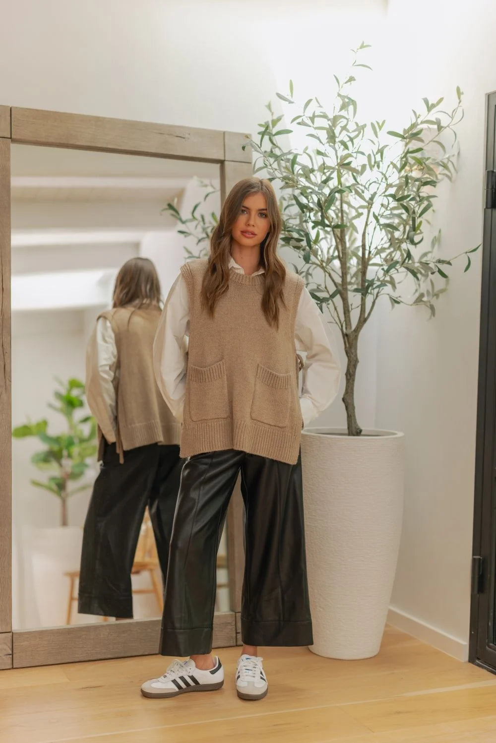 Beige sleeveless vest with pockets and white Adidas sneakers on wide straight leg leather pants